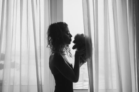 silhouette of a girl and a small furry dog on the background of the window. the concept of loving and caring for Petsの写真素材