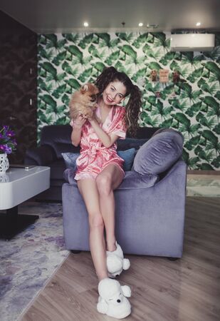 girl in a dressing gown holds a small spitz in her hands at homeの写真素材