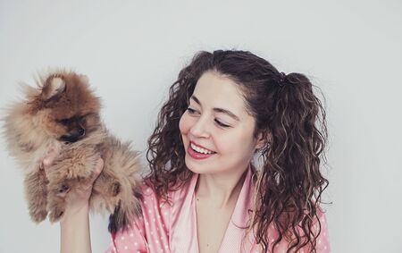 Pleased happy girl gets lovely puppy, plays and embraces four legged friend with love. Woman hugs Pomeranian spitz.の写真素材