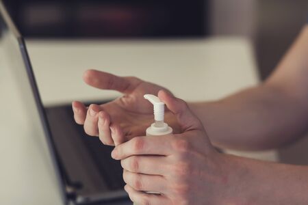 Coronavirus. Working from home on notebook. Freelancer. Cleaning her hands with sanitizer gelの写真素材
