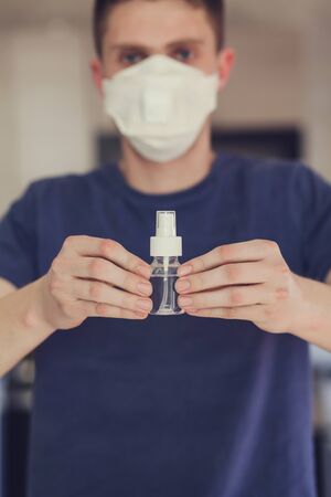 Man in medical protective mask with an antibacterial spray for hands disinfection. Health protection prevention during flu virus outbreak and coronavirus epidemicの写真素材