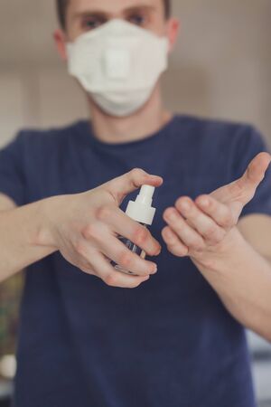 Man in medical protective mask with an antibacterial antiseptic for hands disinfection in home.の写真素材