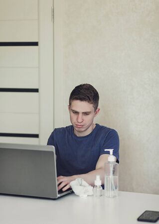 man works at a computer at home during the quarantine. On the table is an antibacterial gel and a protective maskの写真素材