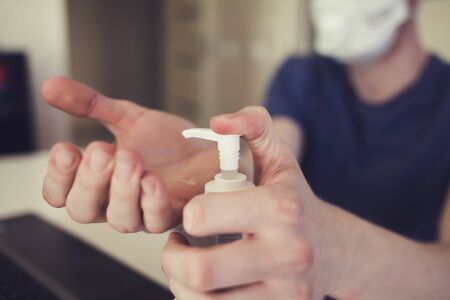 man in a mask at home puts an antibacterial gel on his handsの写真素材