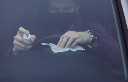 man in a black protective mask disinfects the car. the taxi driver sprays the car after the customerの写真素材