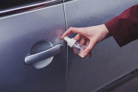 Hand of  is man spraying alcohol, disinfectant spray on handle of car door,safety,prevent infection...