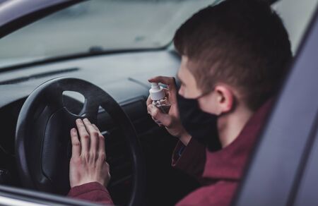 Man spraying antibacterial sanitizer spray on steering wheel, disinfection car. Prevent Coronavirus, COVID-19. Male wearing in black protective mask driving a car.の写真素材