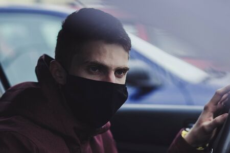 Portrait of man wearing disposable medical facemask in a car during coronavirus outbreak.の写真素材
