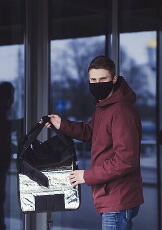 Delivery pizza on quarantine. Young man with black mask holding bag with pizzaの写真素材