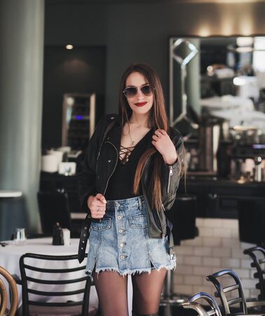Gorgeous young woman wearing black leather jacket posing in empty cafe. Beauty, fashion concept.の写真素材