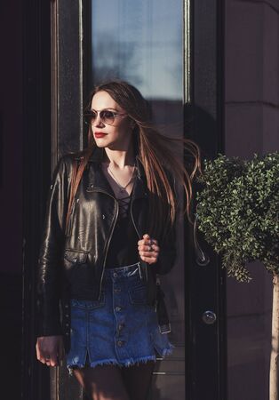 fashionable lady in a leather jacket and sunglasses poses in an urban settingの写真素材