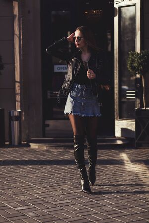 Elegant brunette woman in leather jacket walking on city streetsの写真素材