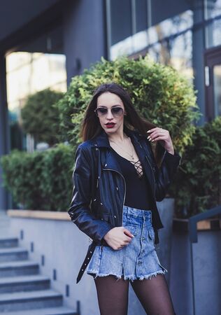 Beautiful young woman in leather jacket and denim skirtの写真素材