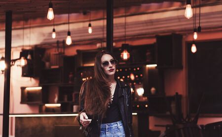 Fashion style portrait of young beautiful woman in black leather jacket walking at city streets.の写真素材