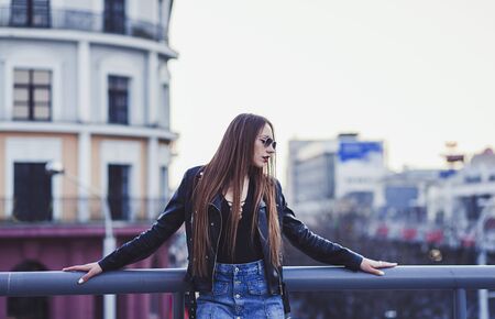 beautiful lady in a leather jacket and skirt at sunset on the background of the cityの写真素材