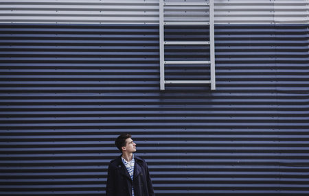 Young stylish man dressed in jacket stands against wall. Space for text