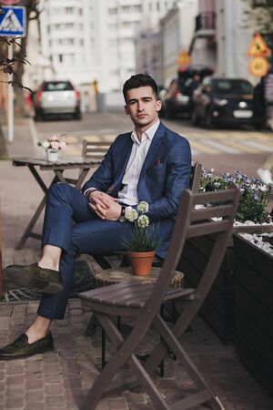 Young stylish handsome businessman model in suit sitting in the street. High fashion lookの写真素材