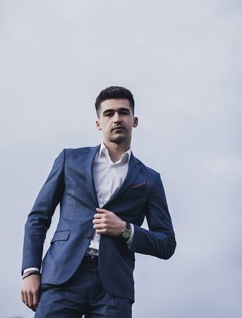 Fashionable young handsome businessman wearing suit and watch on sky backgroundの写真素材