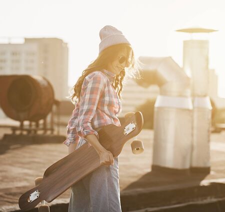 Funky girl with skate on sunset. Stylish woman holding longboardの写真素材