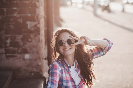 Surprised emotional hipster girl in urban style. Brunette curly woman sitting on skateboardの写真素材