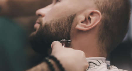 Close-up view of young bearded man getting beard haircut by hairdresser at barbershopの写真素材