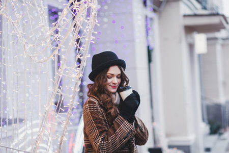Lifestyle fashion portrait of stunning girl. Wearing stylish coat and drinking coffee in city