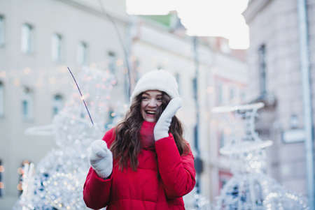 beautiful young woman in winter clothes and hat holding a sparkler and looking at the cameraの写真素材