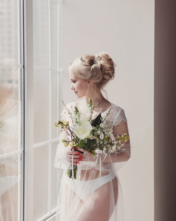 Wedding. Beautiful bride indoors with bouquet of flowers looking at cameraの写真素材