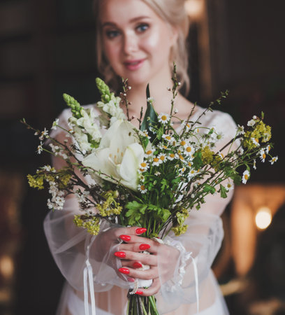 Bride morning preparation. Beautiful bride in white wedding negligee sitting in bedroomの写真素材