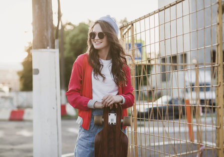 an active woman in a hat rides a longboard in the city at sunsetの写真素材