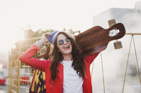 an active woman in a hat rides a longboard in the city at sunsetの写真素材