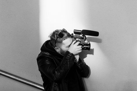 Handsome stylish man with beard in sunglasses and leather jacket posing near wallの写真素材
