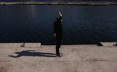 Young fit man stretching out his arms stretches outdoors against the background of the river