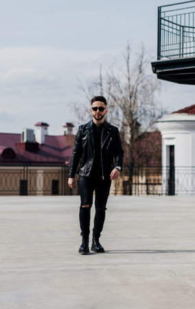 Good looking man in sunglasses and leather jacket in street. Spring trends. Monochrome image