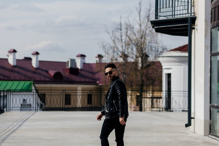Good looking man in sunglasses and leather jacket in street. Spring trends. Monochrome image