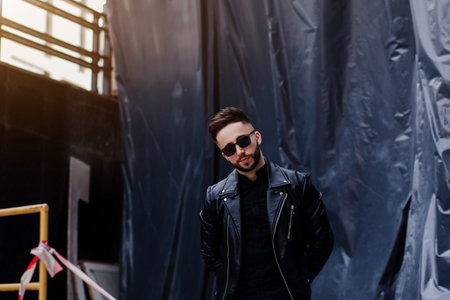 young man is wearing a leather jacket and sunglasses while looking at the camera. street styleの写真素材