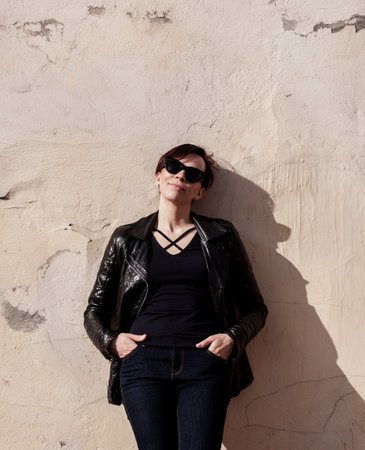 fashion female model in sunglasses and black leather jacket posing in cityscape. black and white photoの写真素材