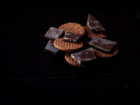 baked round chocolate chip cookies and pieces of chocolate on a black table, close upの写真素材