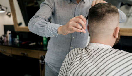 Barber making haircut of attractive bearded man in barbershop. Process of haircutsの写真素材