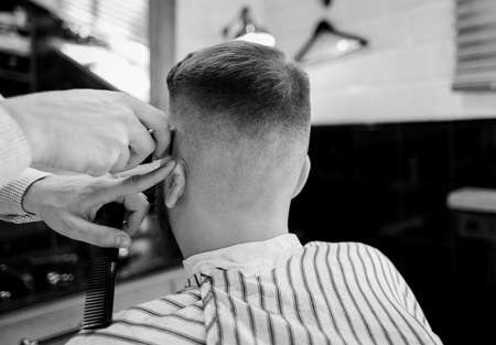 Barber trim hair with clipper on man in barbershop. Professional hairdresser cut hair with electric shearer machine on guy. black and white photoの写真素材