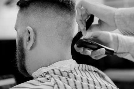 Barber trim hair with clipper on man in barbershop. Professional hairdresser cut hair with electric shearer machine on guy. black and white photoの写真素材