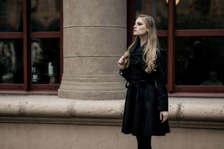 glamorous lady in a black coat and ankle boots poses on the steps in the cityの写真素材