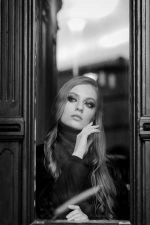 Beautiful girl behind the glass, portrait of young woman in window, concept of female emotions. black and whiteの写真素材