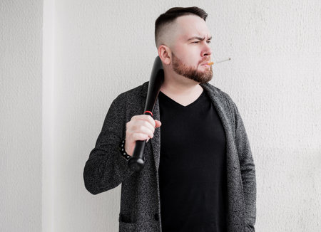 a close-up portrait of a man of a bearded man with a bat and a cigarette. criminal elementの写真素材