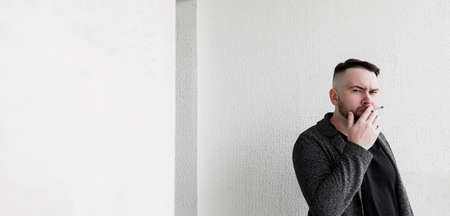 young handsome bearded hipster man smoking cigarette near wall. copy spaceの写真素材