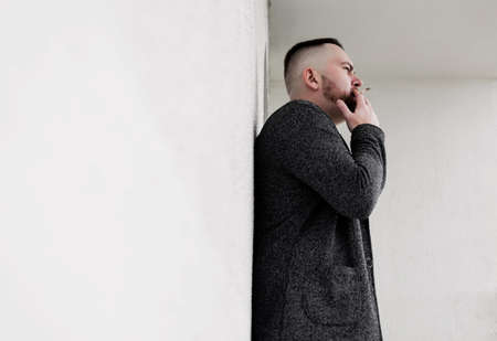 young handsome bearded hipster man smoking cigarette near wall. copy spaceの写真素材