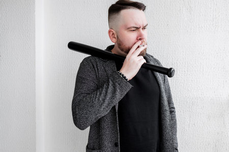 bad boy with a cigarette. a man holds a baseball bat. criminal conceptの写真素材