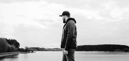 man in a leather jacket near the river stands and looks into the distanceの写真素材