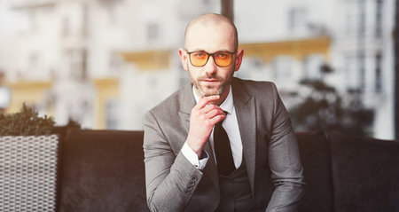 Handsome young businessman in glasses looking at camera and sitting in officeの写真素材