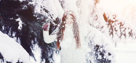 Cute young woman playing with snow in fur coat outdoors